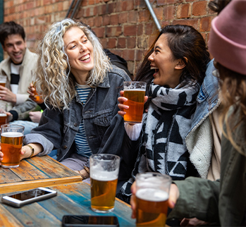 two women laughing with each other holding glasses of beer