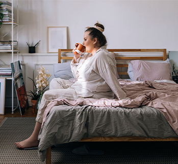 woman in her pajamas sitting in bed holding a mug