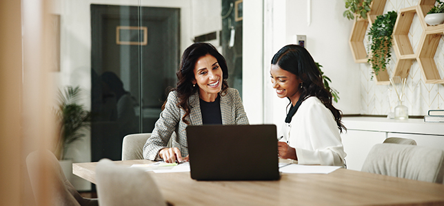 Two women sitting at a table looking at a laptop