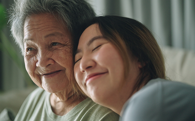 Two people sitting closely together indoors, with one person resting their head against the other's shoulder.