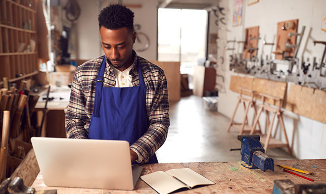 Man wearing blue apron and plaid shirt looking at laptop