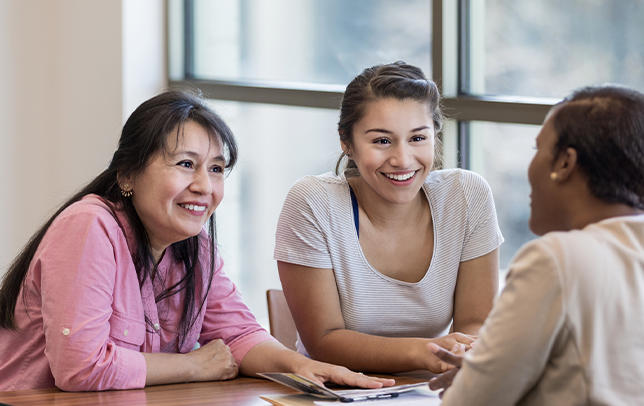 Three women sitting at table.  Two women are facing camera and the one woman has her back to the camera.