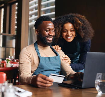 Woman and man holding credit card looking at laptop in restaurant