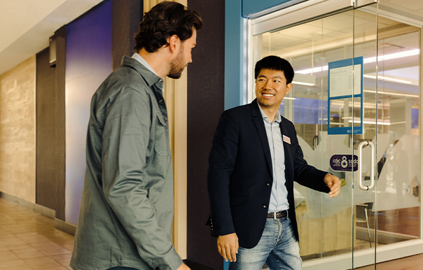 Two people meeting at the entrance to a glass-walled office space, with one person holding the door open.