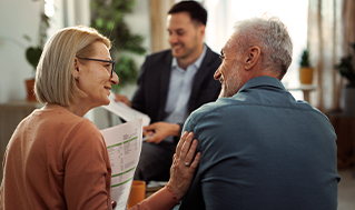 Financial advisor meeting with two clients seated together and discussing printed financial documents.