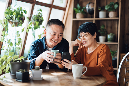 Older man and woman sitting at table with mugs looking at mobile device