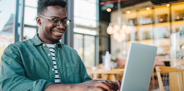 man wearing glasses and green shirt sitting looking at a laptop