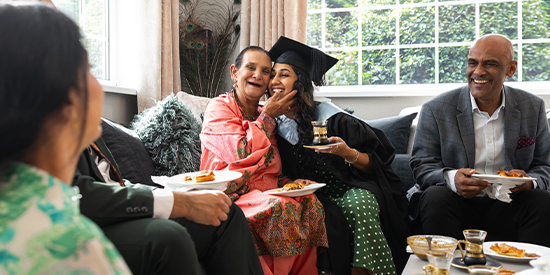 A joyful family gathering celebrating a graduate sharing food and smiles in a bright living room.