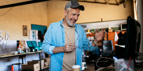 Smiling man in blue shirt holding spectacles while looking at a monitor