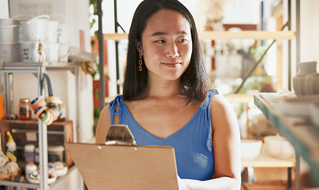 Smiling woman wearing a blue dress holding a clipboard.