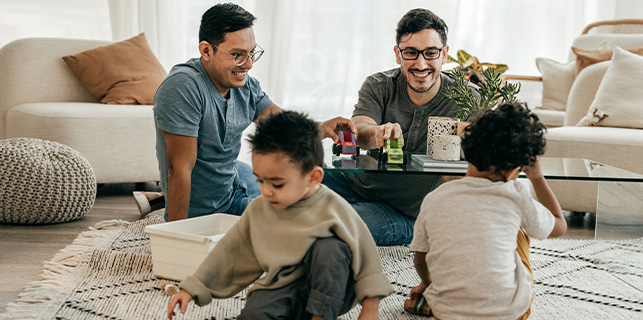 two men wearing glasses sitting at a coffee table playing with two toddler age children